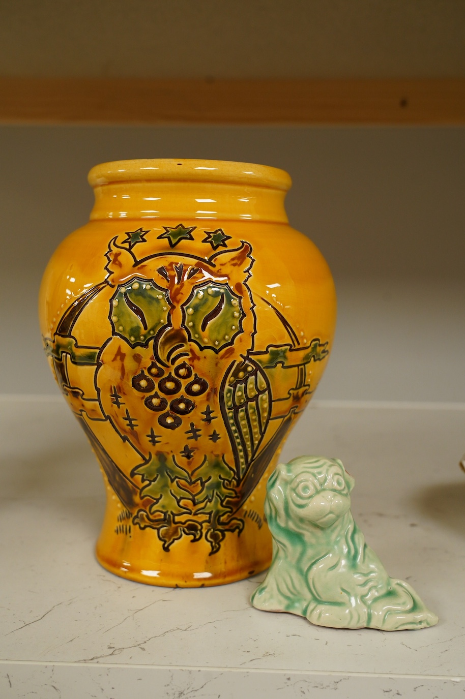 A Brannam yellow vase with stylised decoration of a standing owl with a background of the moon, clouds and three stars, 21cm high, and a Brannam, Barnstaple, a shade of green stylised sitting Dog of Fo, 7.5cm high. Condi